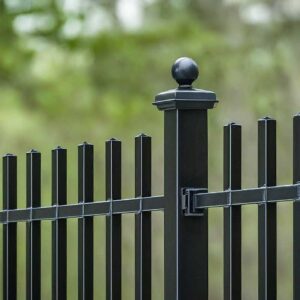 A sleek black aluminum fence with pointed pickets and decorative finials stands tall around a backyard patio, offering a stylish and secure boundary.