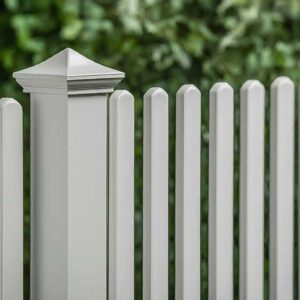 Close-up view of a white vinyl picket fence with a decorative post cap.